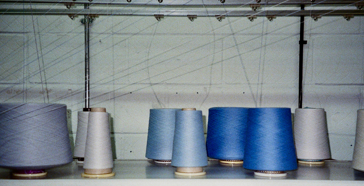 Cashmere yarn cones in shades of blue, grey and cream arranged on a shelf in a knitwear factory.