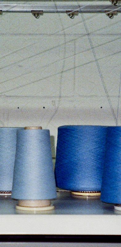 Cashmere yarn cones in shades of blue, grey and cream arranged on a shelf in a knitwear factory.